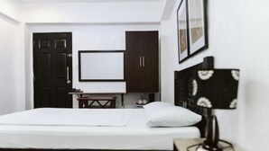 A bedroom with a bed, a desk, a chair, a TV, and a lamp. - San Agustin Residences (Makati)