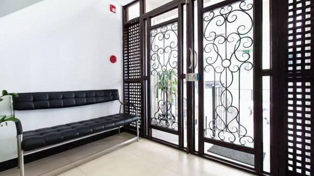 A waiting area with a black cushioned bench, a white chair, and a decorative metal gate. - San Agustin Residences (Makati)