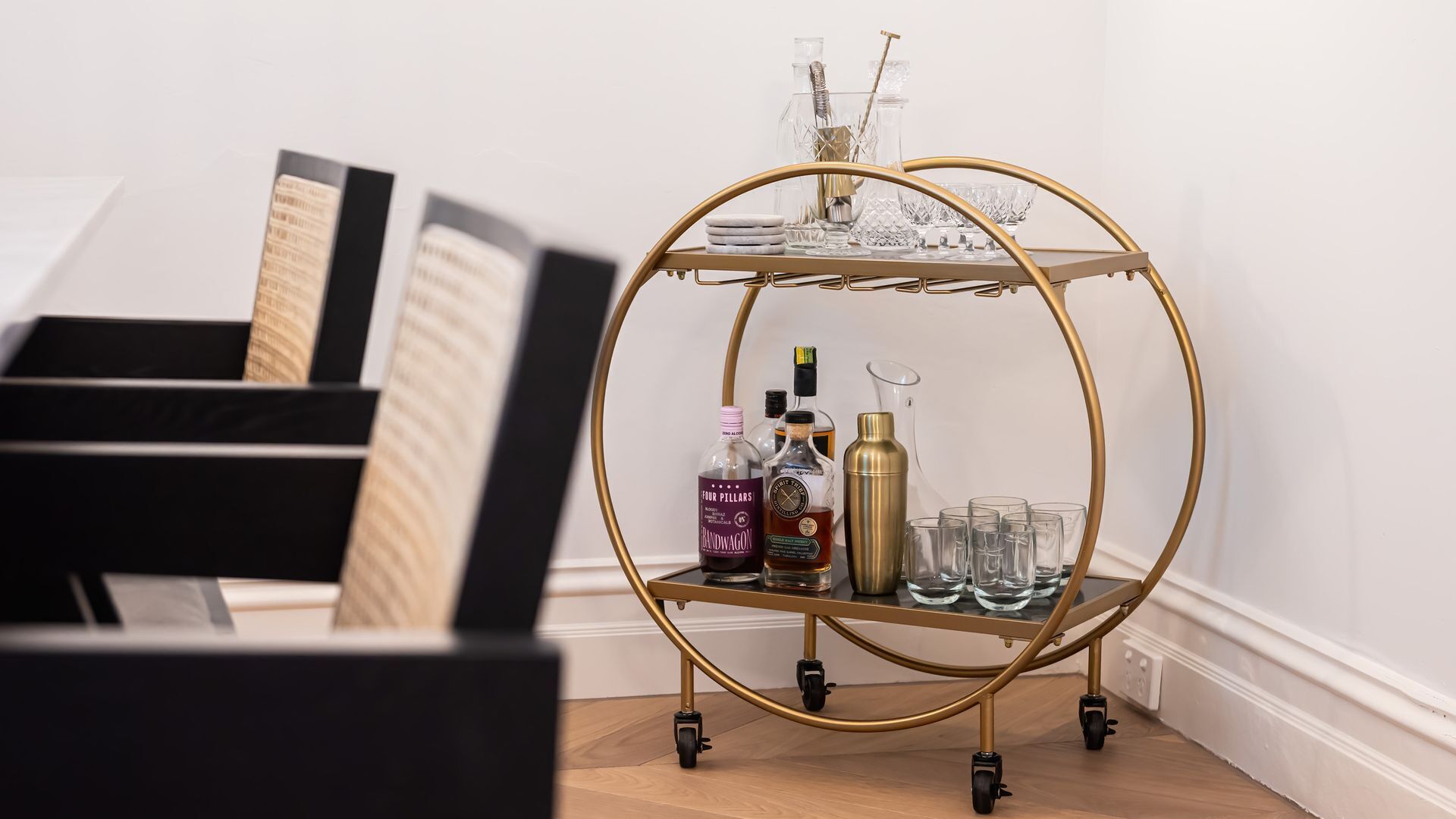 Un chariot à cadre doré, contenant des bouteilles d’alcool et des verres, est placé près d’un piano.
