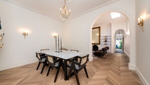 Een eetkamer met een marmeren tafel, donkere stoelen, een kroonluchter en wandlampen.