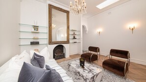 Een moderne woonkamer met een open haard, glazen schappen, een grote spiegel en een kroonluchter.