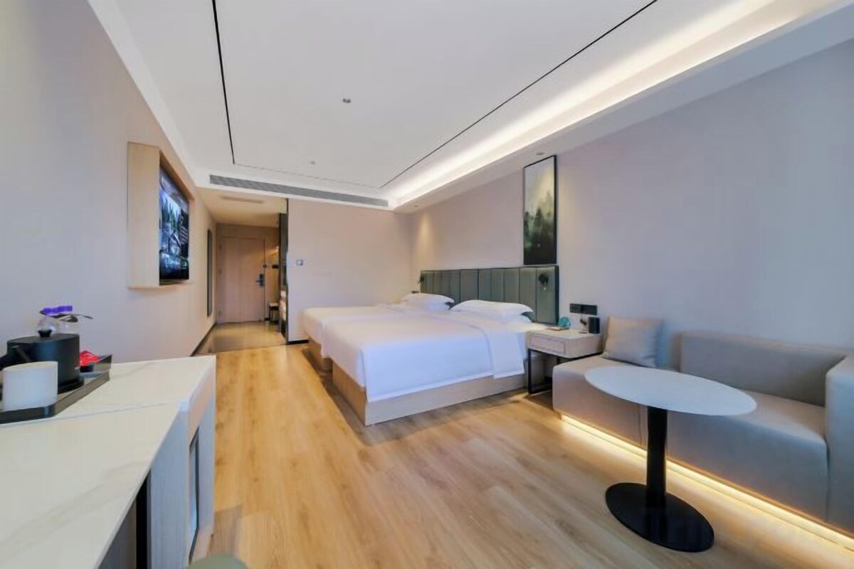 Una habitación de hotel moderna con una cama grande, una mesita de noche, una pequeña mesa redonda, un sofá y un televisor montado en la pared.