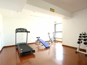 Un gimnasio con cinta de correr, banco y estante para pesas.