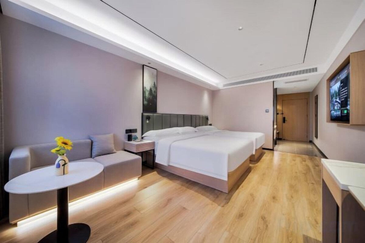 Una habitación de hotel moderna con una cama, un sofá, una mesita con un jarrón y un televisor en la pared.