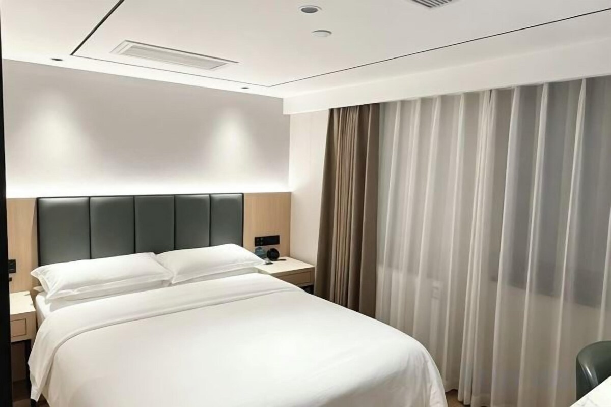 Una habitación de hotel con cama, mesita de noche y cortinas.