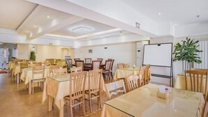 Ein geräumiger Konferenzraum mit mehreren Tischen und Stühlen, einer Whiteboard-Tafel und einem Blumentopf.