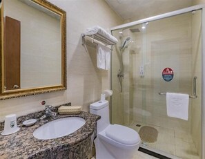 Ein Badezimmer mit Marmorwaschtisch, Toilette in Weiß, einer Duschkabine und einem großen Spiegel mit goldener Rahmung.