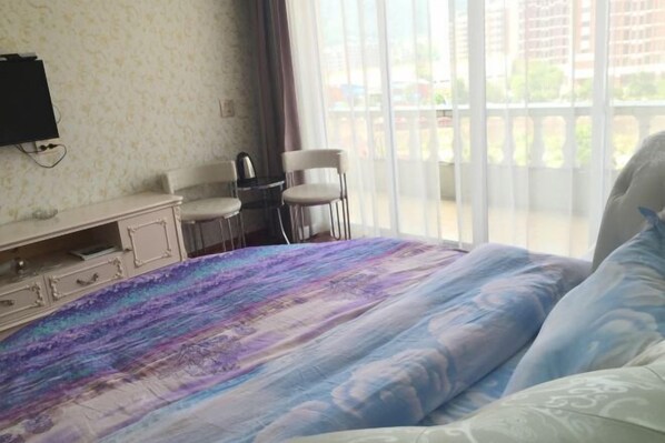 Ein Schlafzimmer mit einem Bett, einem an der Wand befestigten Fernseher, einem Sessel und einem Blick ins Freie durch ein Fenster.