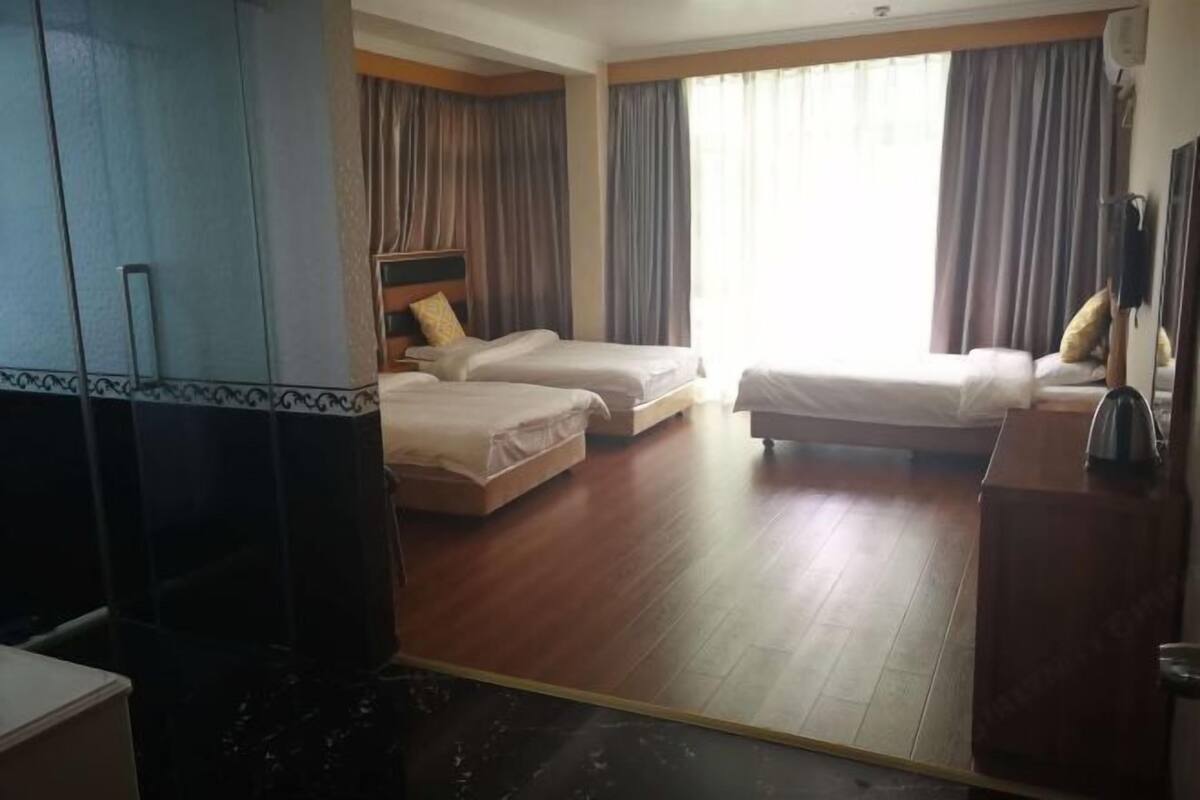 Ett hotellrum med två sängar, ett trägolv, ett stort fönster med gardiner och en garderob.