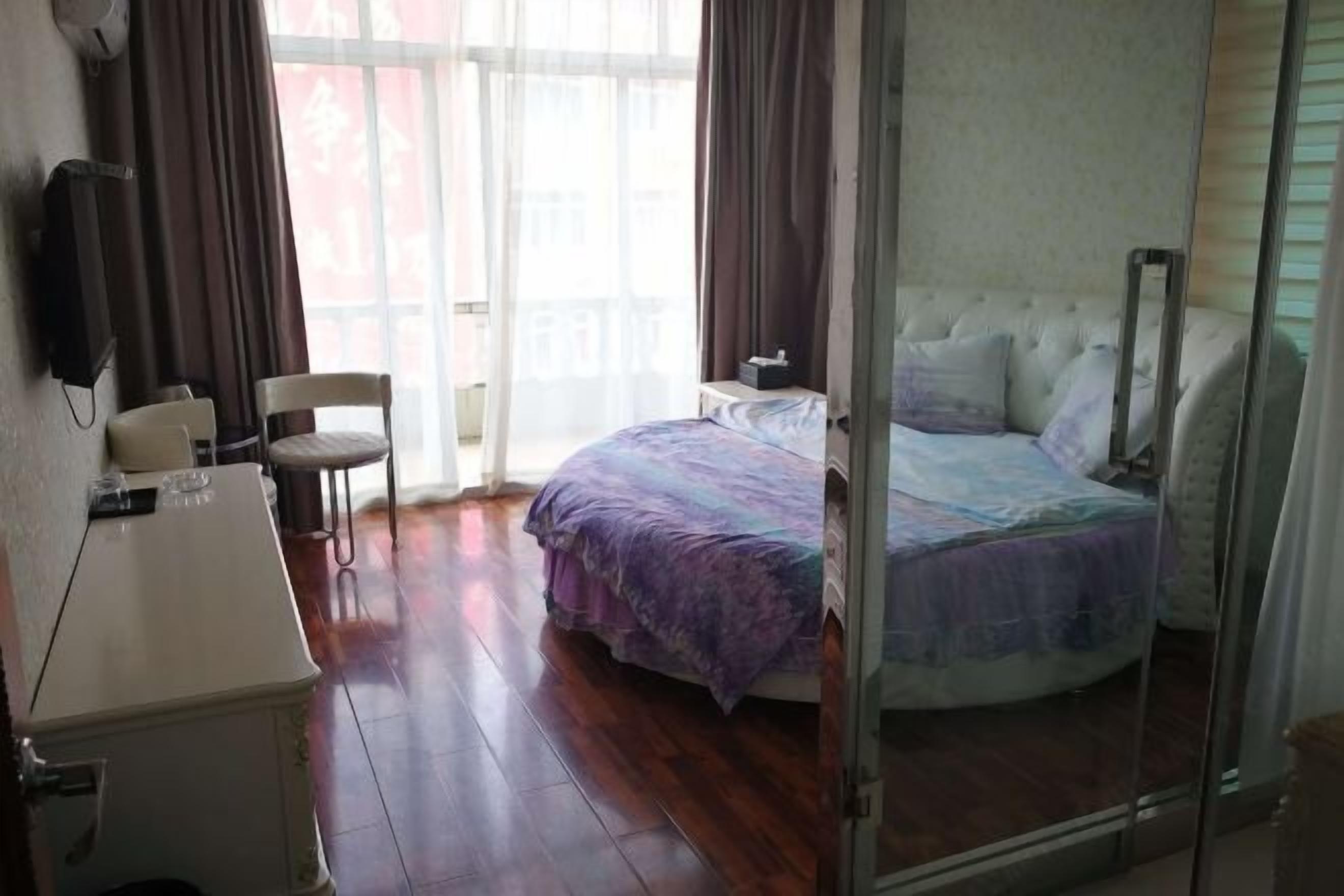 A bedroom with a bed, a desk, a chair, and a window with curtains.