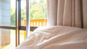 A bedroom with a large window, a wooden deck outside, and a view of greenery.