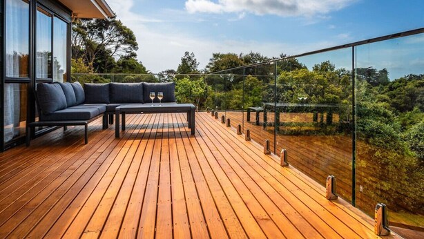 A wooden deck with a sofa and table, overlooking a lush garden and trees.
