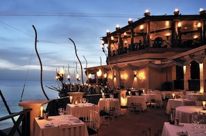An outdoor dining area with tables set for guests, overlooking the sea.