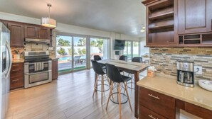 A modern kitchen with wooden cabinets, stainless steel appliances, and a dining area with a pool view. - Mid Century Modern near STRIP w Pool King Suite (Las Vegas)