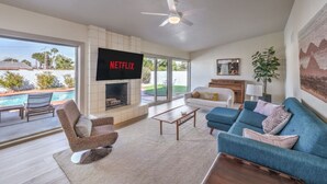 A living room with a fireplace, a TV mounted on the wall, a sofa, a coffee table, and a view of a swimming pool. - Mid Century Modern near STRIP w Pool King Suite (Las Vegas)