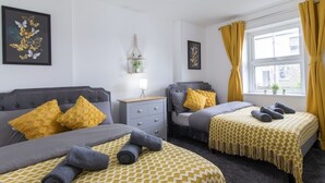 A hotel room with two beds, a bedside table, a lamp, and a window with curtains. - Open Mind Property - Cosy Apartment with 3 Beds (Portsmouth)