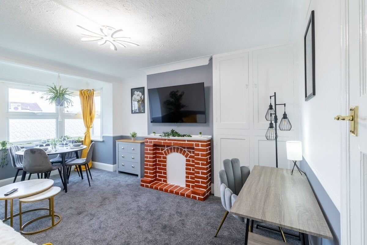 Ein modernes Wohnzimmer mit Kamin aus Ziegelsteinen, einem Essbereich mit rundem Tisch und einem an der Wand montierten Fernseher.