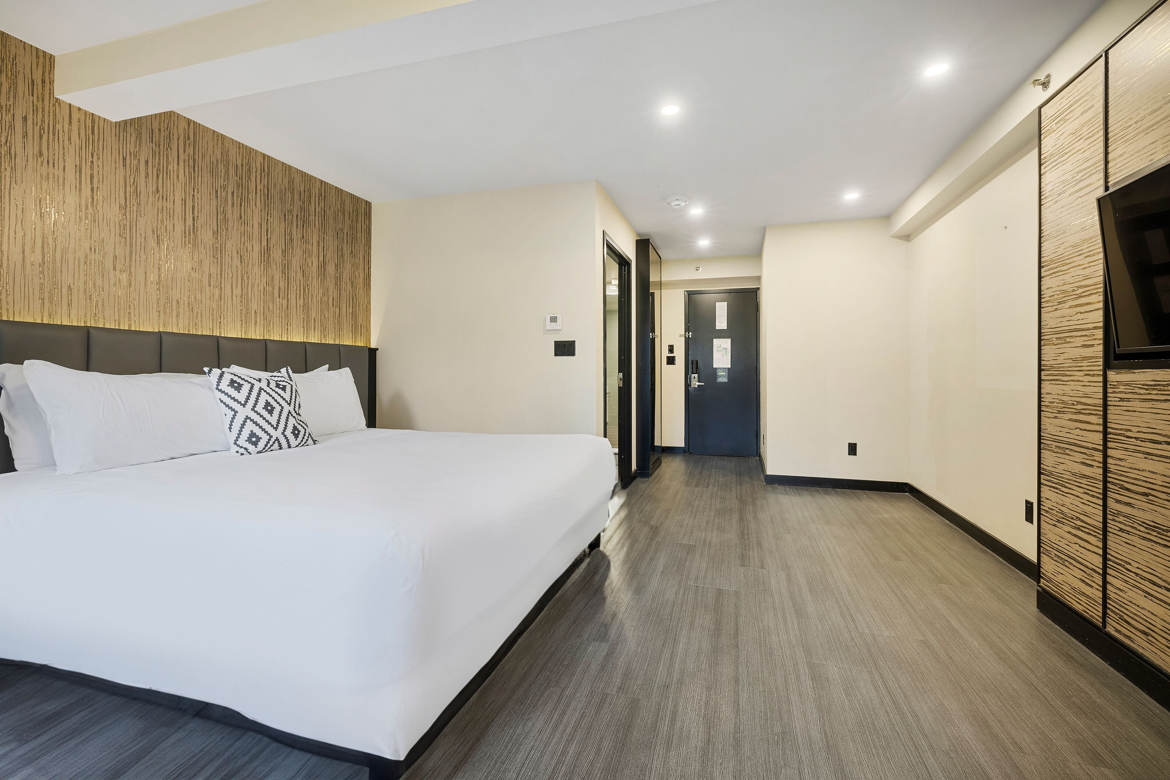 Una habitación de hotel moderna con una cama grande, un cabecero de madera, un televisor de pantalla plana y un vestidor.