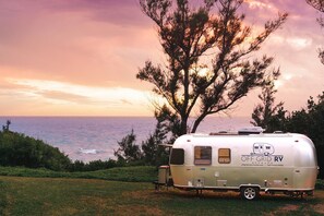 A white RV with 'OFF GRID RV' branding parked on grass, overlooking the ocean.