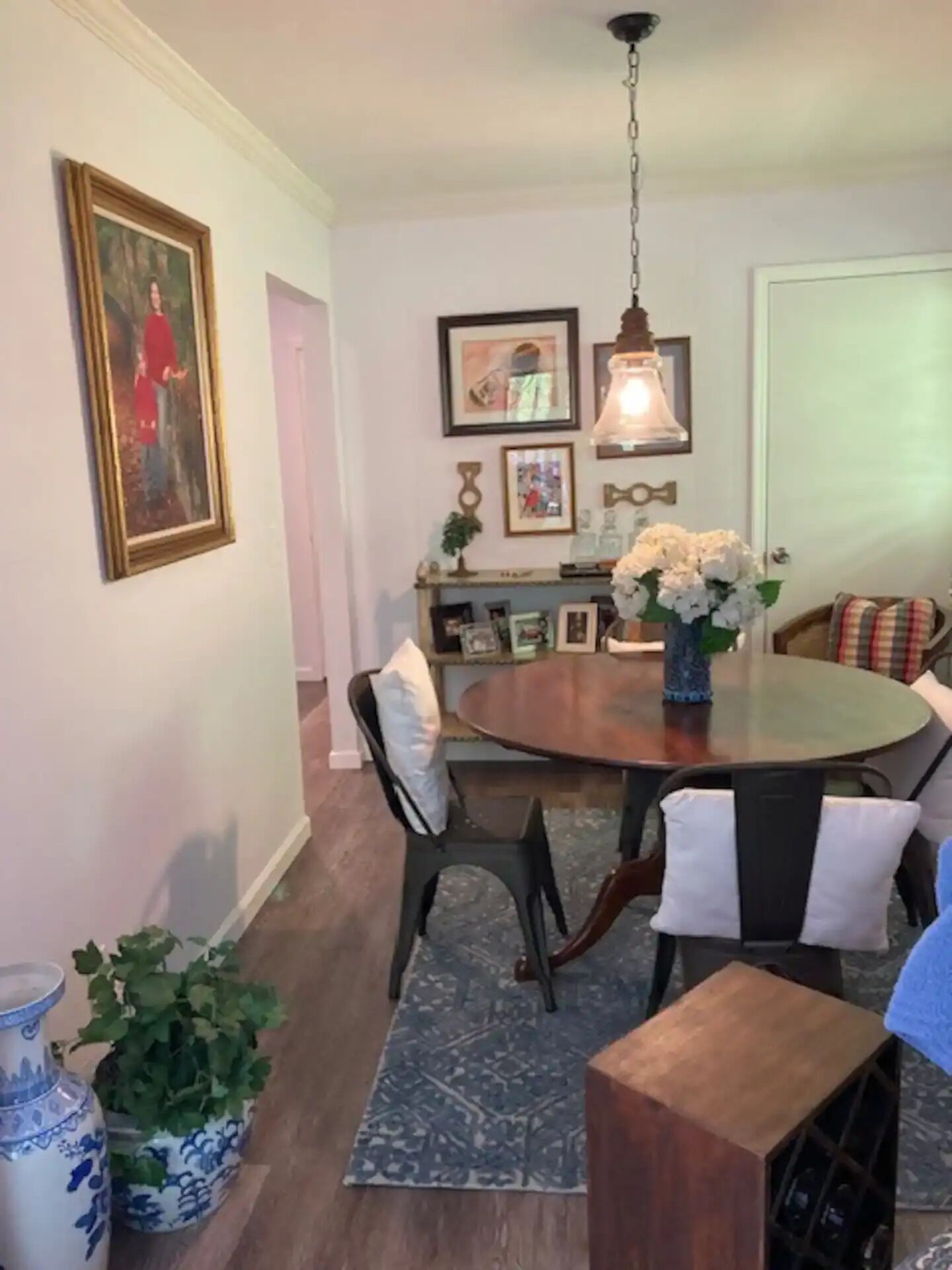 A dining area with a round table, chairs, a vase of flowers, and framed pictures on the wall.