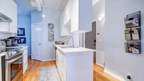 A modern kitchen with white cabinetry, a built-in oven, a sink, and a small island. There is a wooden floor and a light-colored rug. - The Art Loft - A Luxurious 2-BdRm in the Heart of Historic Downtown Wilmington (Wilmington)