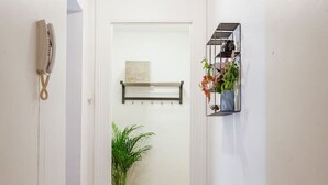 Un couloir avec un banc, un luminaire suspendu, une plante en pot et une étagère avec divers objets.