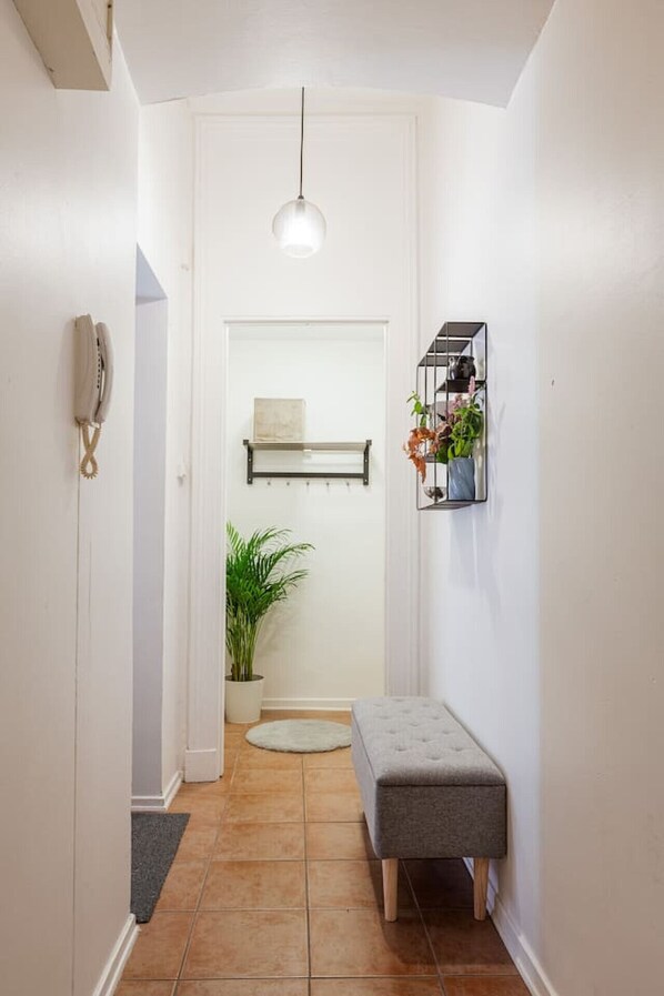 A hallway with a bench, a hanging light fixture, a potted plant, and a shelf with items.