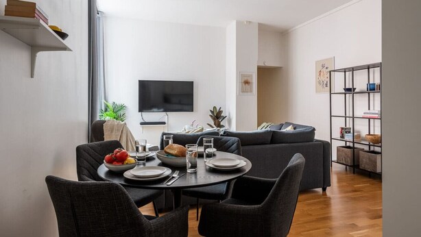 Un salon moderne comprenant un coin repas, un téléviseur à écran plat fixé au mur et une bibliothèque.