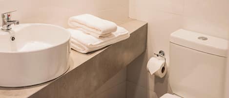 Un baño con lavamanos blanco, toallas apiladas y un inodoro.