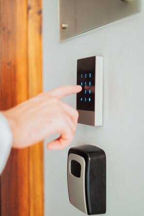 A person using a numeric keypad on a wall-mounted device, likely a door lock or intercom.
