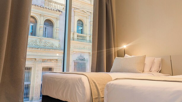 A hotel room with two beds, a large window with curtains, and a view of a historic building. - RentUp Suites Salta (Salta)
