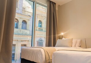 A hotel room with two beds, a large window with curtains, and a view of a historic building. - RentUp Suites Salta (Salta)