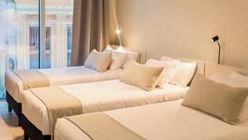 A hotel room with two beds, a large window with a view of a building, and a bedside lamp.