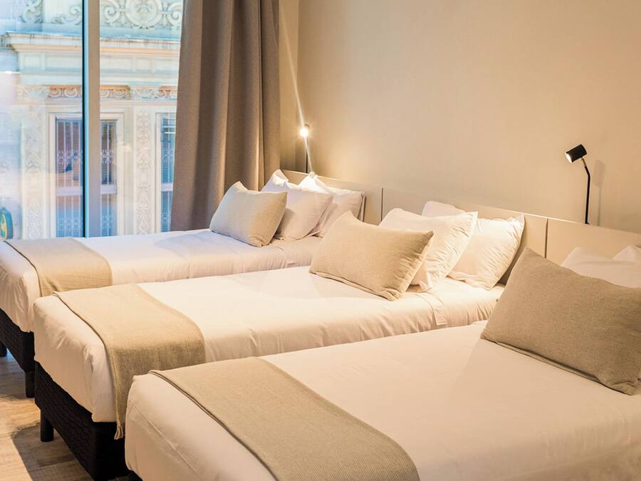 A hotel room with two beds, a large window with a view of a building, and a bedside lamp.