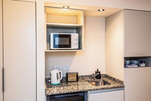 Una cocina compacta equipada con microondas, hervidor de agua, tostadora y pileta.