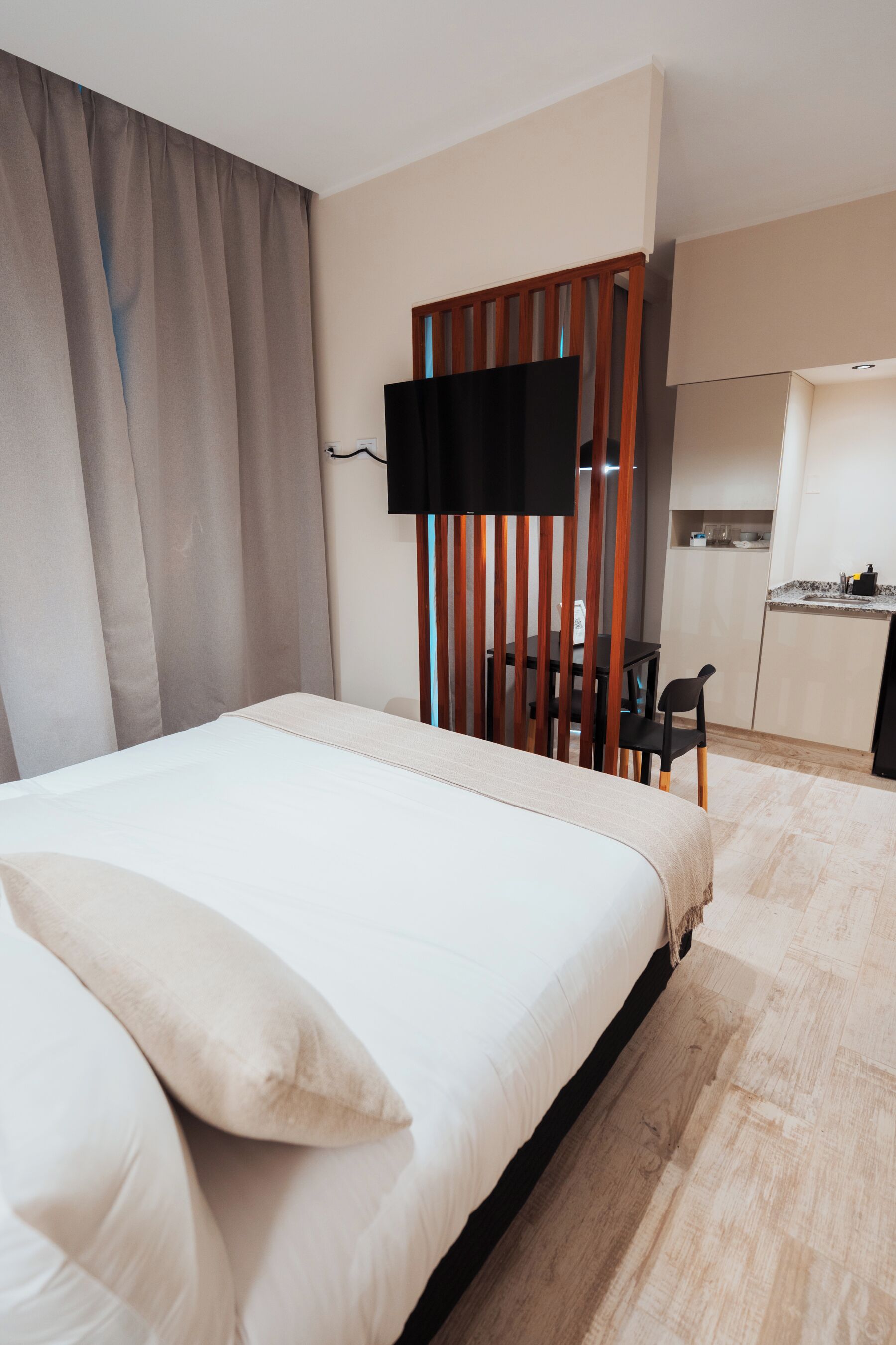 Habitación de hotel con una cama, un escritorio, una silla y un televisor instalado en una separadora de madera.