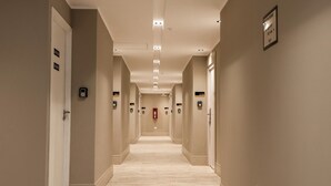 A hotel hallway with a light-colored floor and walls, multiple doors, and emergency exit signs. - RentUp Suites Salta (Salta)