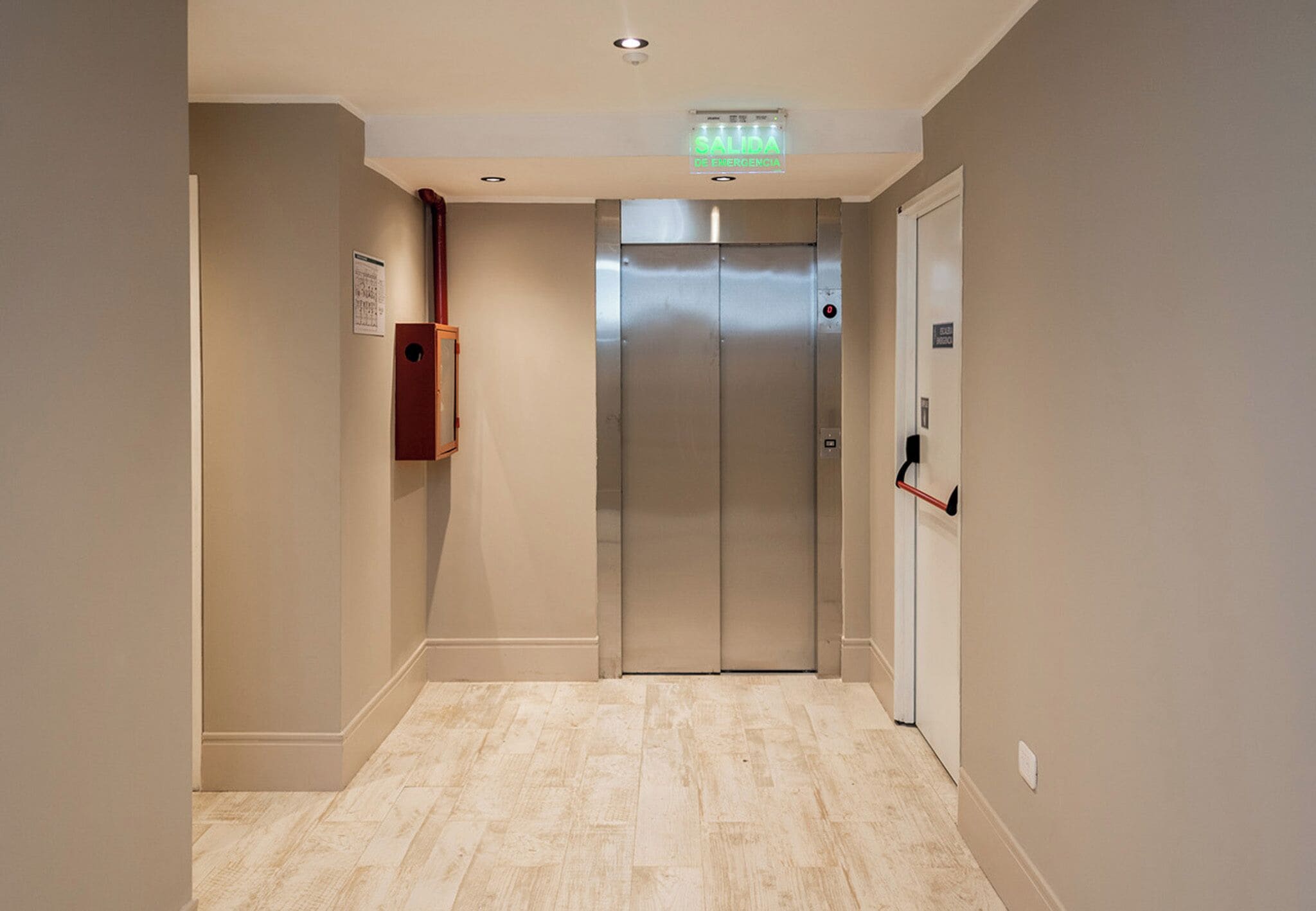 A modern elevator in a hallway with a light wood floor and beige walls.
