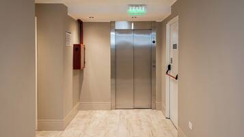 A modern elevator in a hallway with a light wood floor and beige walls.