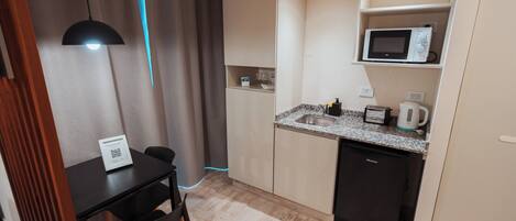 Cocina compacta con microondas, lavamanos y una pequeña zona de comedor con mesa y sillas.