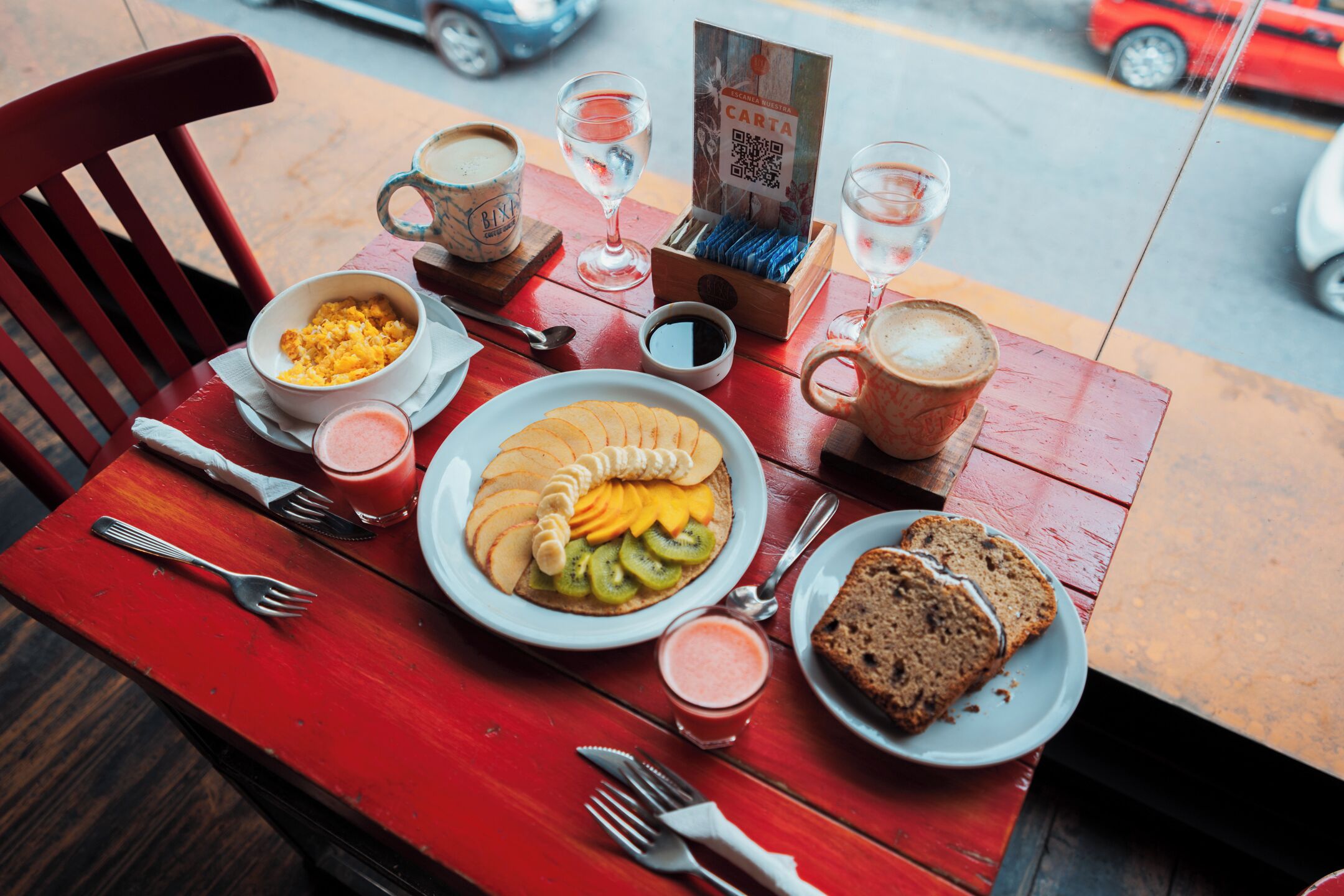 A dining table with a red chair, plates of food, cups, and cutlery.