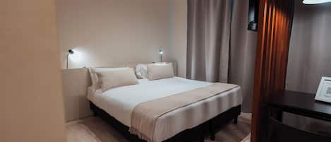 A neatly arranged bedroom with a bed, bedside lamps, a desk, and a curtain.