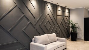 A modern interior with a grey sofa against a geometric wall design, a potted plant, and a tiled floor. - RentUp Suites Salta (Salta)