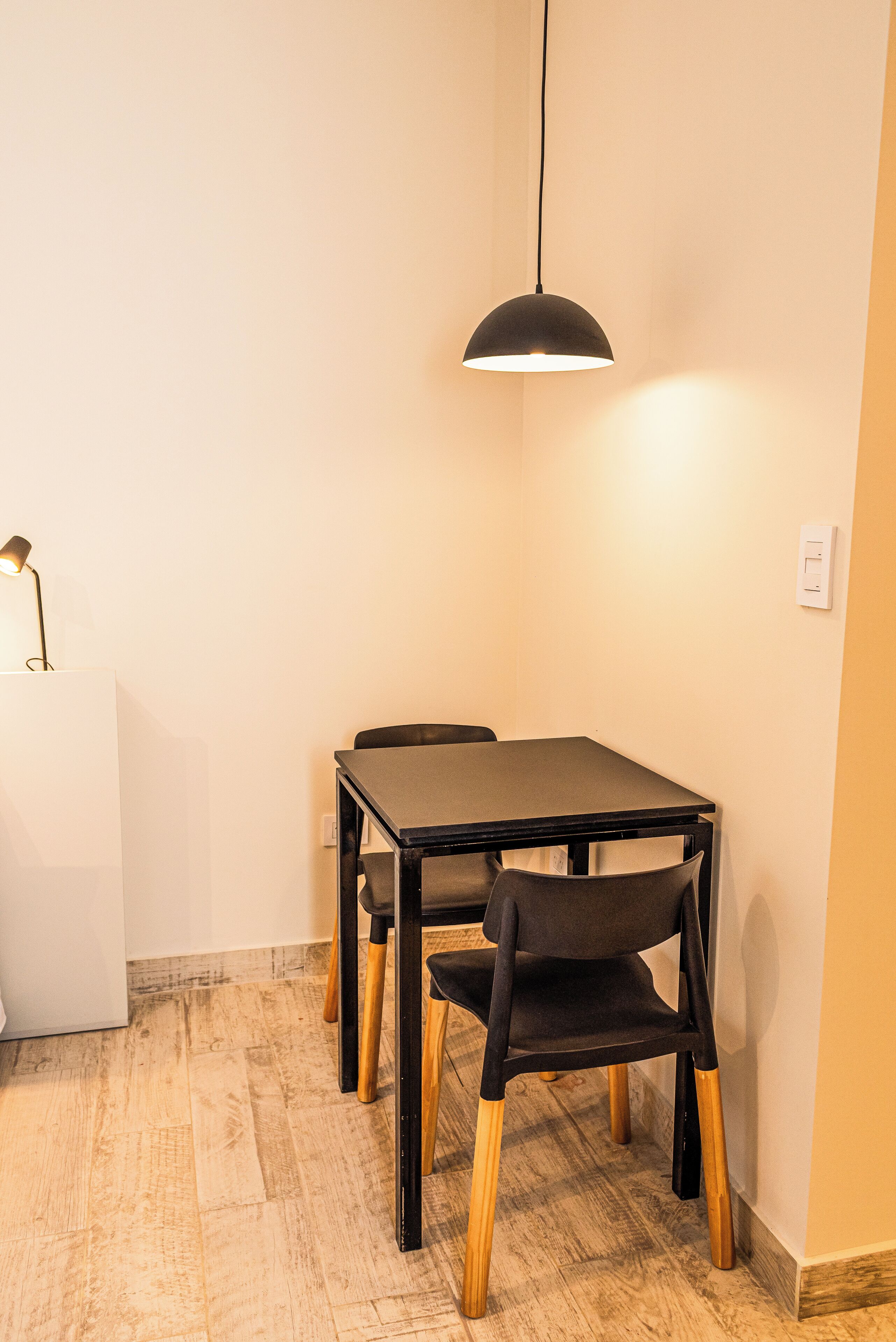 Uma área de refeições com mesa, cadeiras, uma lumin ária pendente e um balcão branco.