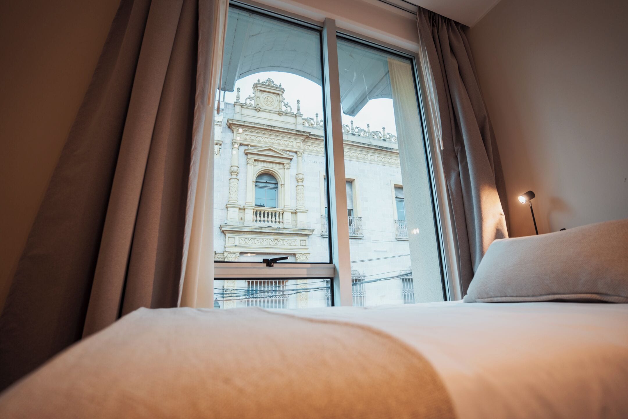 Une chambre d’hôtel avec une grande fenêtre, un lit et une lampe.