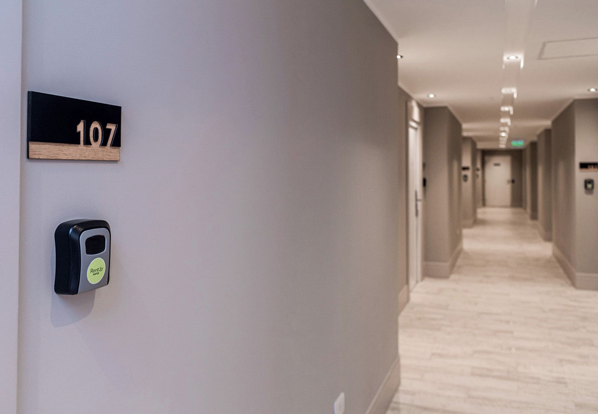 A hallway with a sign indicating room number 107, a door with a keycard reader, and a light-colored floor.