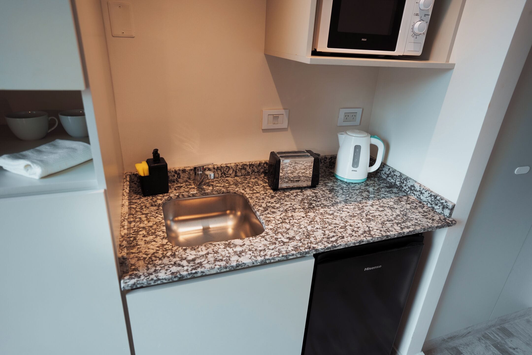 A compact kitchen with a granite countertop, a stainless steel sink, a toaster, a kettle, and a microwave.