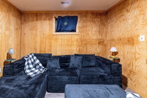 Ett rum med träpanel på väggarna, en soffa i mörk färg, två sidobord med lampor och ett litet fönster med en gardin.