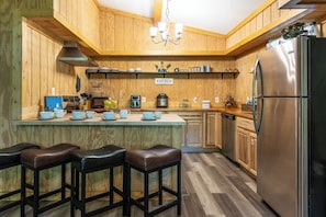 Una cocina con paredes de madera, un refrigerador de acero inoxidable, una cafetera y un letrero que dice 'KITCHEN'.
