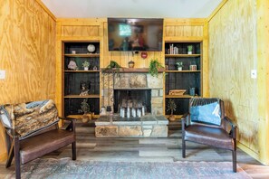 Una sala de estar acogedora con chimenea de piedra, dos sofás de cuero, estanterías de madera con libros y adornos, y un televisor montado en la pared.